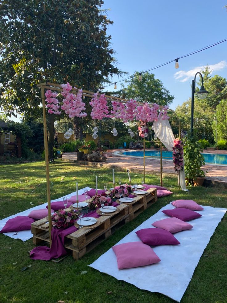 a table set up with pink pillows and place settings for an outdoor dinner by the pool