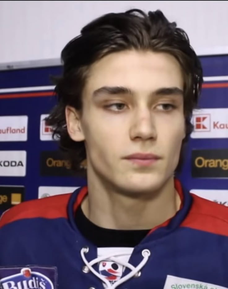 a young man in a blue and red jersey is looking at the camera while standing next to a wall