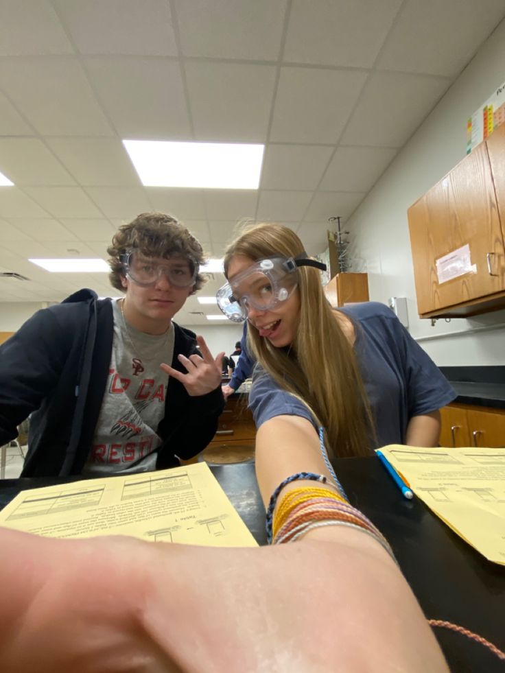 two people standing in front of a table with papers on it and one person pointing at the camera