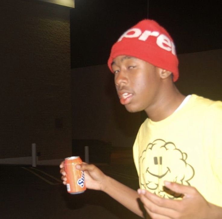 a young man in a yellow shirt and red hat is holding a can of soda