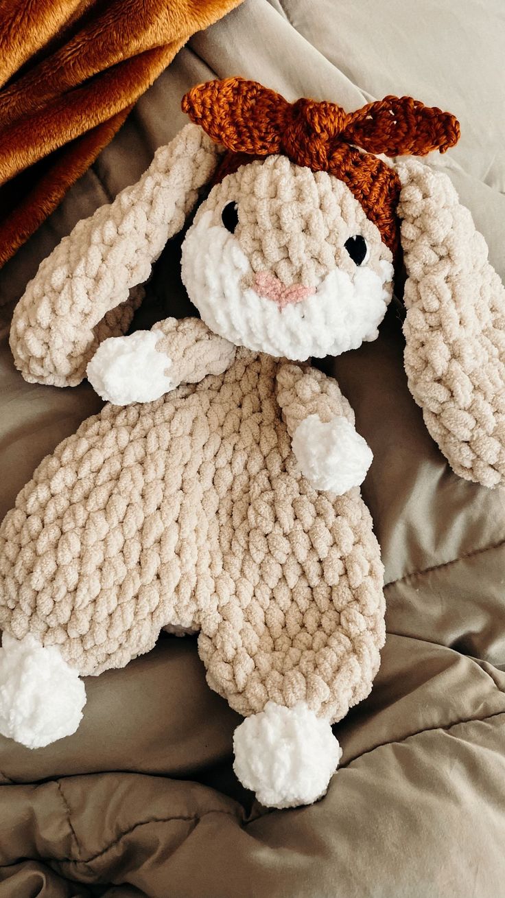 a crocheted bunny laying on top of a bed next to a brown blanket