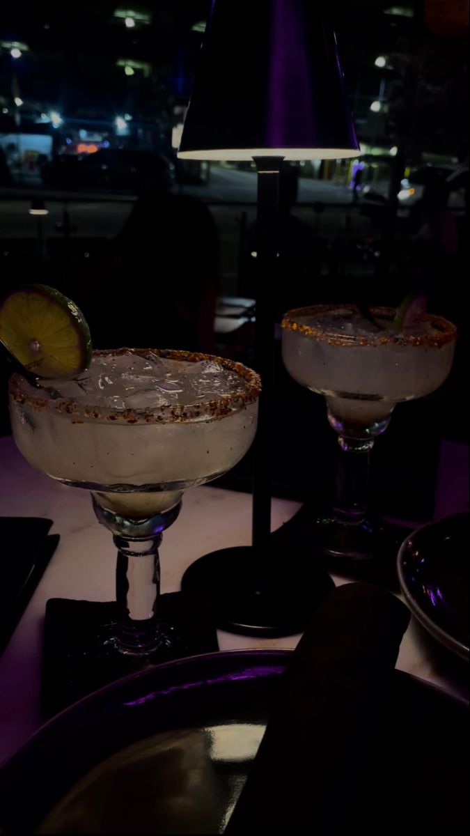 two martinis sitting on top of a table in front of a window at night