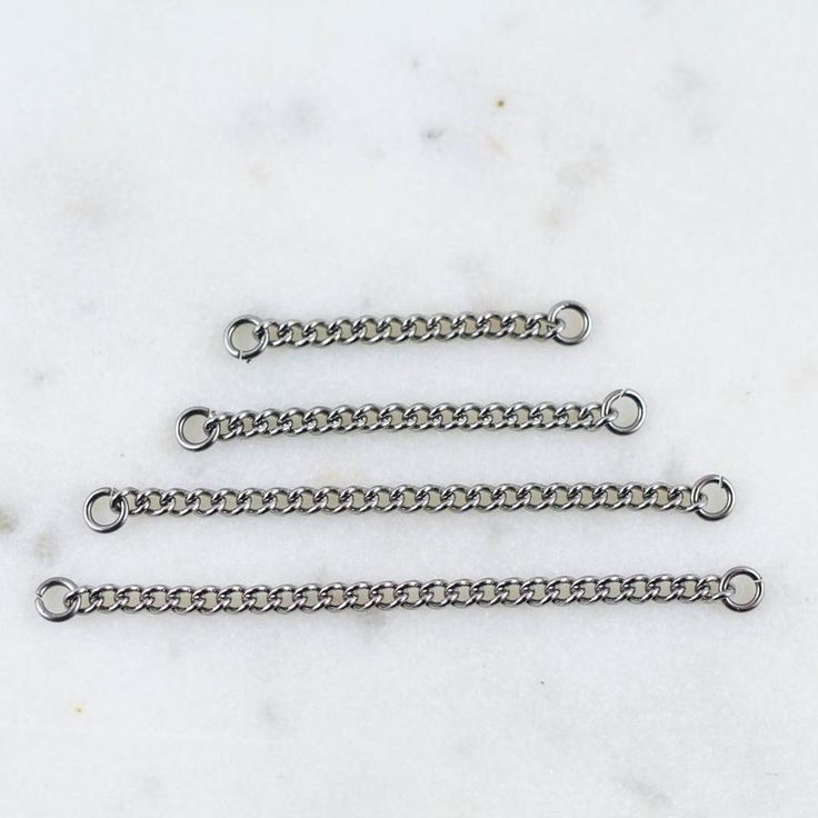 three silver chains sitting on top of a white marble countertop next to each other