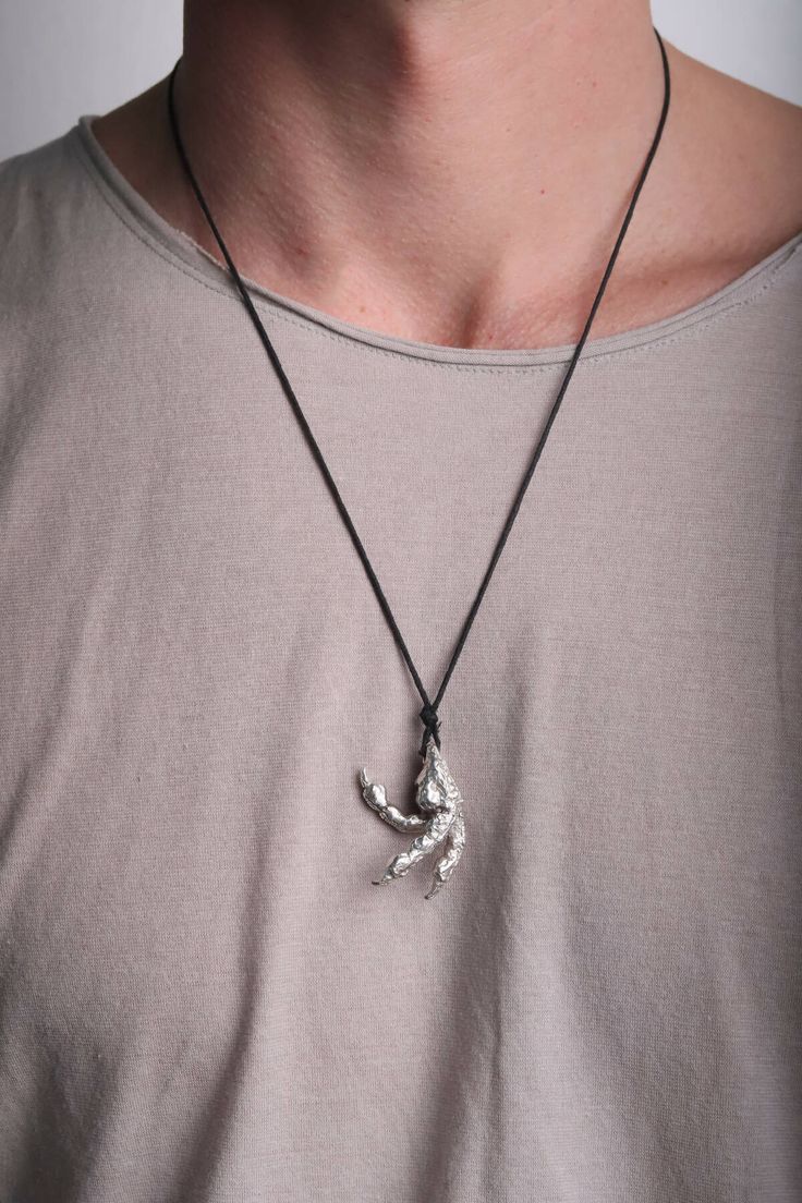 The Raptor Paw Necklace with Black Neck Cord is a unique and eye-catching piece of jewelry that is sure to catch the eye of anyone who wears it.The raptor paw, made with attention to detail, it is in silver.The shape is extremely realistic, with a texture similar to animal skin and a sharp shape at the base like a real dinosaur paw.The black cord is strong and flexible, and can be easily adjusted to the desired length thanks to its adjustable closure. Additionally, the black cord contrasts well Hand Cast Metal Amulet Necklaces, Hand Cast Metal Pendant Jewelry, Hand-cast Metal Pendant Jewelry, Hand Cast Metal Amulet Jewelry, Hand Forged Silver Brutalist Jewelry, Brutalist Hand Cast Metal Jewelry, Hand Cast Metal Brutalist Jewelry, Hand Cast Brutalist Metal Jewelry, Brutalist Pendant Jewelry Gift