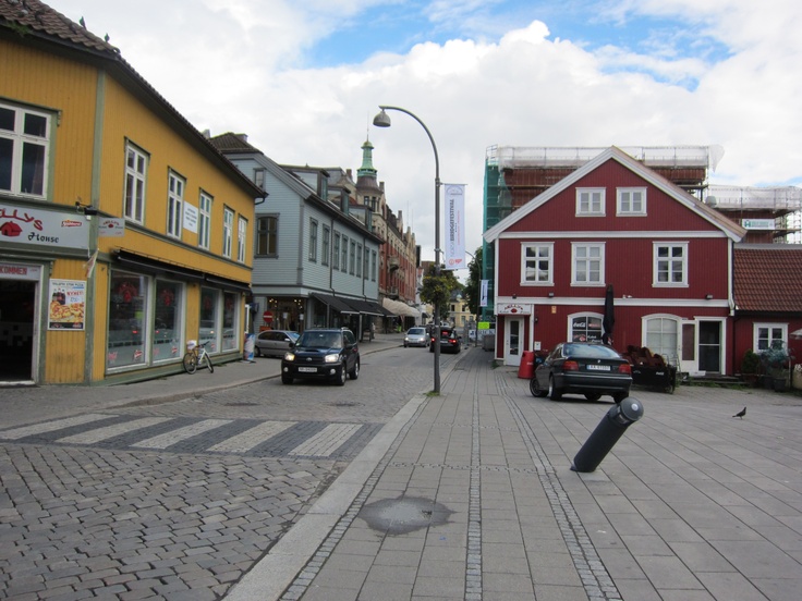 cars parked on the side of a street next to tall buildings and shops in a small town