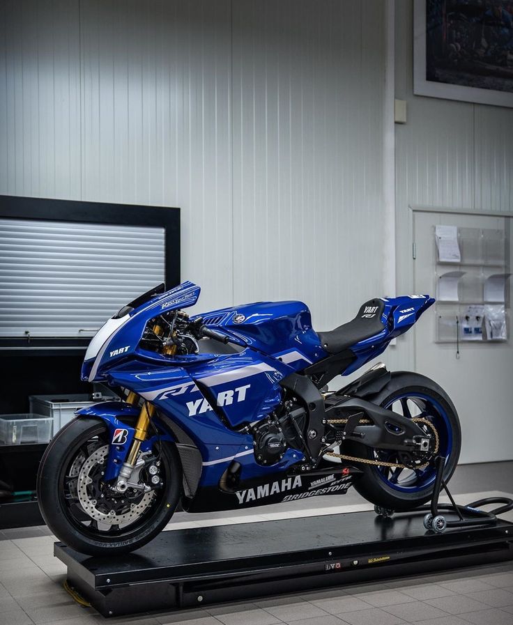 a blue motorcycle parked on top of a black platform in front of a white wall