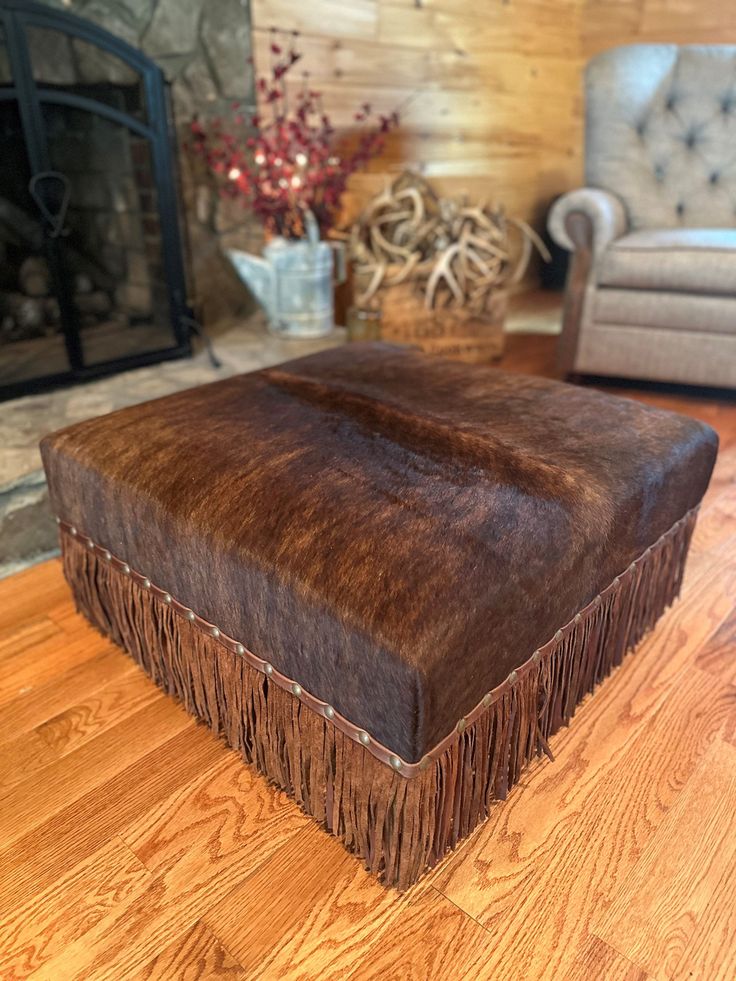 a brown ottoman sitting on top of a hard wood floor next to a fire place