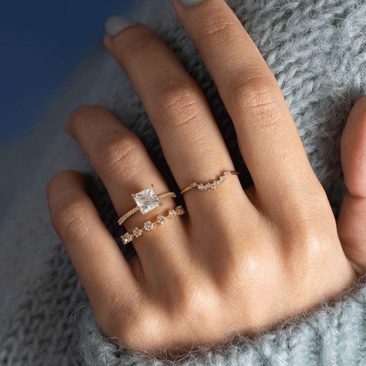 a woman's hand wearing a gold ring with two diamonds on the middle and one diamond in the middle