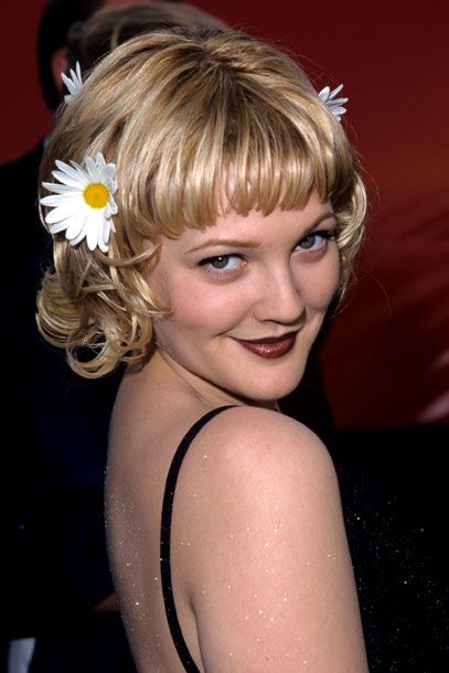 a woman with blonde hair and a flower in her hair smiles at the camera while wearing a black dress