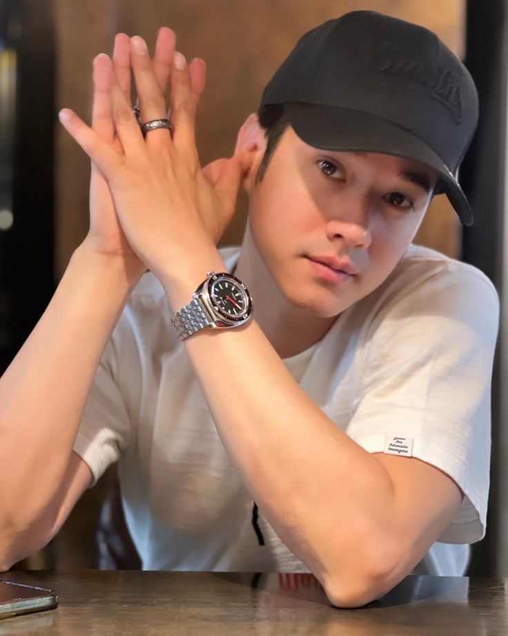 a young man sitting at a table with his hands on his head and wearing a hat