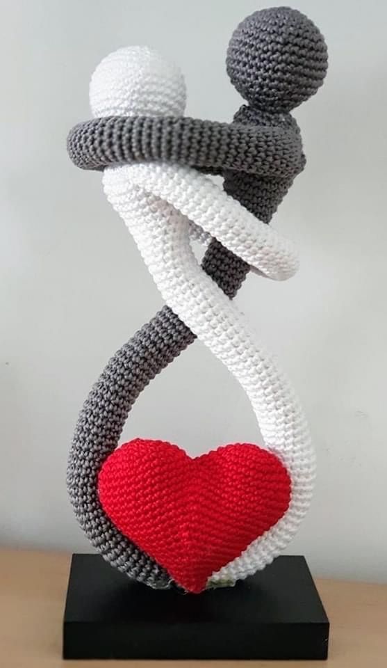 a crocheted sculpture with a red heart in the center and two people holding each other