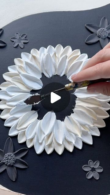 someone is cutting out paper flowers on a black board with white and gray petals in the center