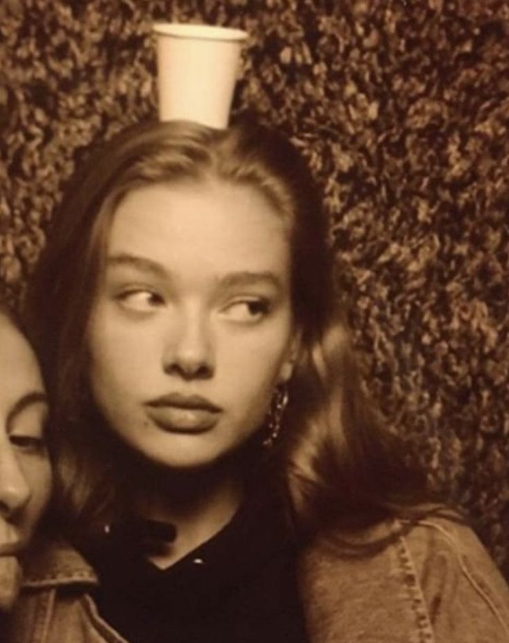 two women are posing for a photo with a cup on top of their head in front of a wall