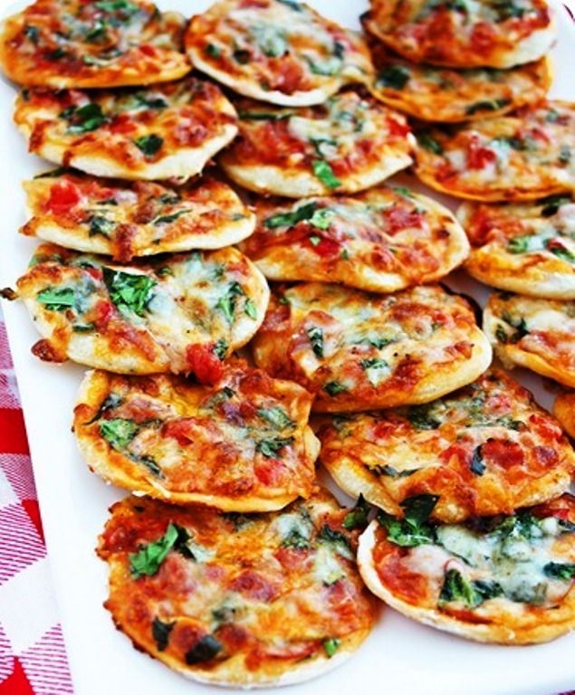 small pizzas with cheese and spinach are arranged on a white platter, ready to be eaten