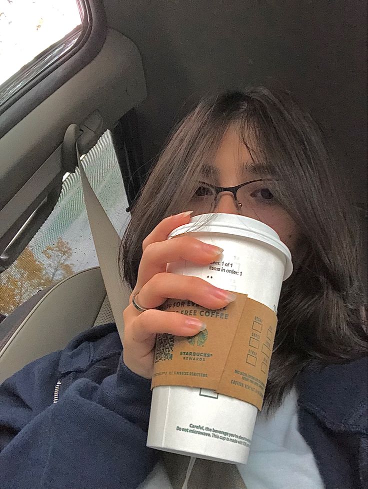 a woman is holding a coffee cup in her hand while sitting in the back seat of a car