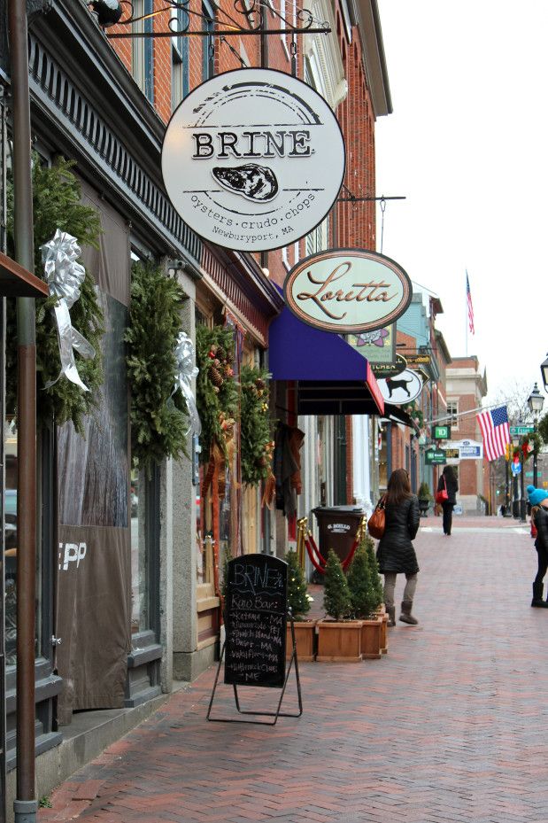 people walking down the sidewalk in front of some shops on a brick street with christmas wreaths