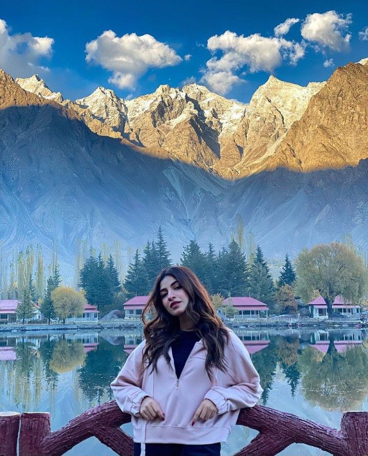 a woman standing next to a lake with mountains in the background