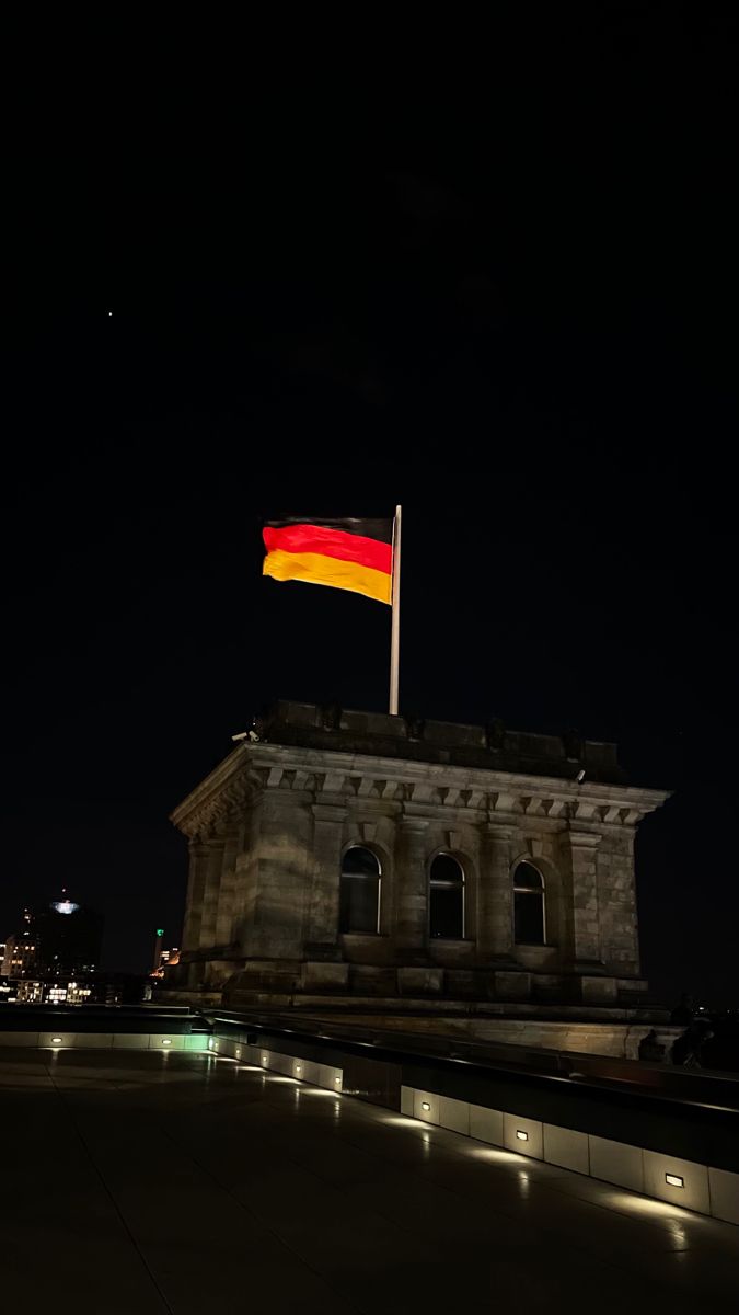 the german flag is flying at night in front of a building with lights on it