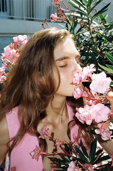 a woman in pink shirt smelling flowers with eyes closed