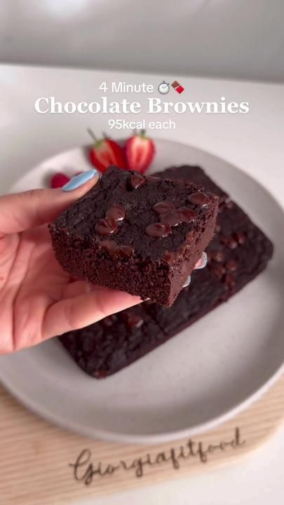 a hand holding a piece of chocolate brownie on a plate