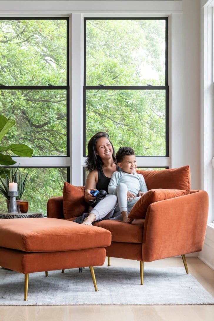 a woman and child sitting on an orange chair in front of a window with trees outside