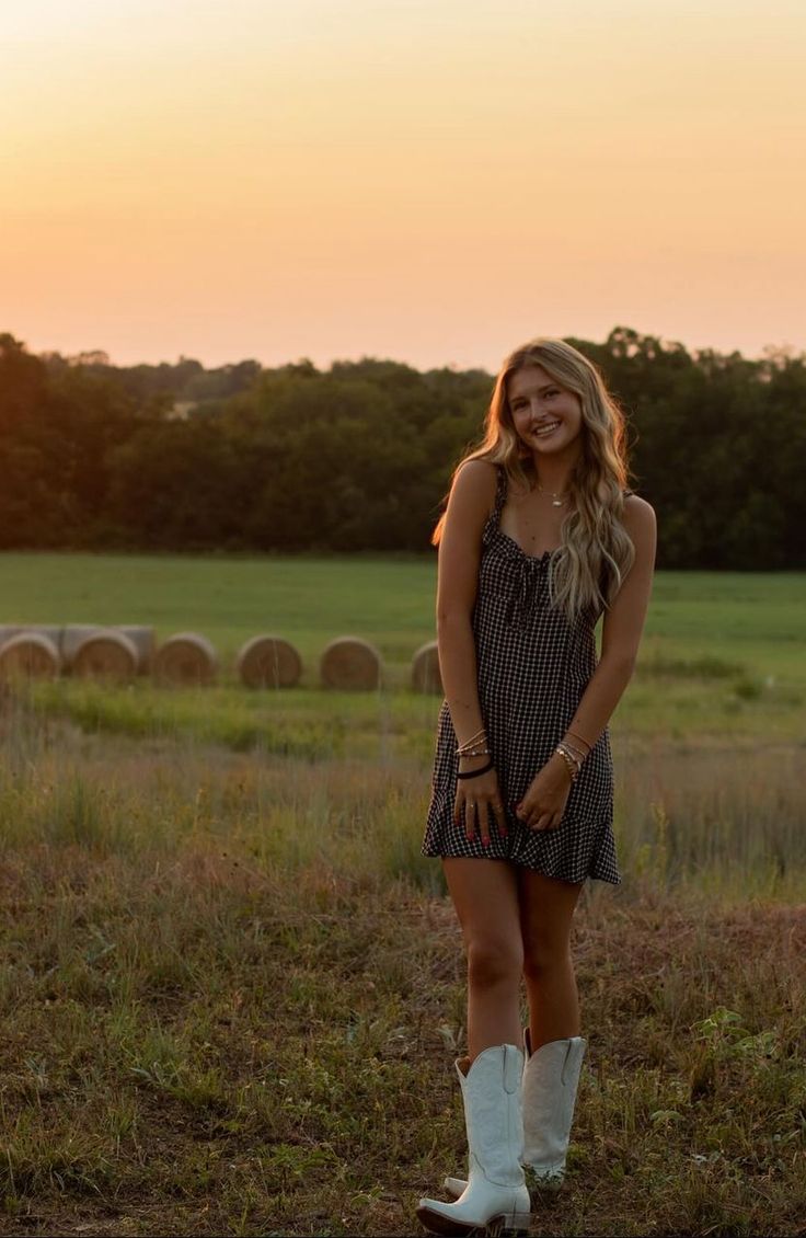 a beautiful young woman standing in a field at sunset wearing white boots and a dress