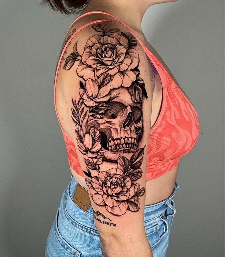 a woman with a skull and flowers tattoo on her upper half sleeve, wearing jeans