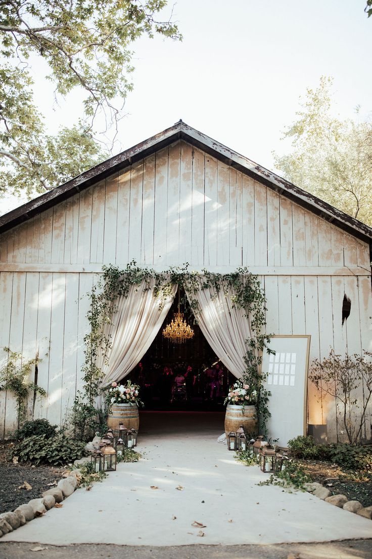 the entrance to a barn is decorated with flowers and greenery for an outdoor ceremony