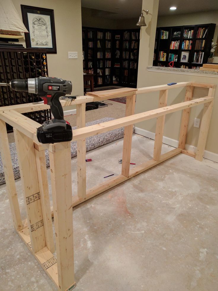 a cordless driller sitting on top of a wooden frame in a room with bookshelves