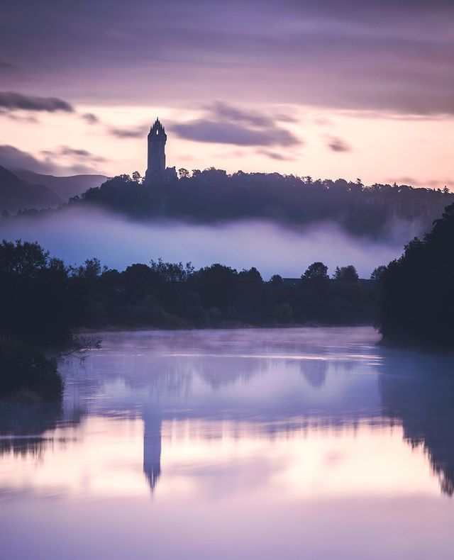 a large tower sitting on top of a hill next to a lake covered in fog