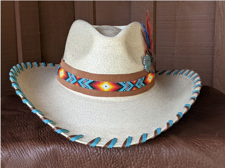 The Nelle starts with a Mexican soft palm leaf hat body that has a 3 3/4" brim and 5 1/4" crown. Hand laced in saddle and turquoise leather lace. The beaded hatband has colors of turquoise and orange and is mounted on tan suede. The back of the band has a deer antler bead for accent. Copper patina Concho and an orange decorative feather completes the hat. Note: Please allow 3-4 weeks. Southwestern Turquoise Hat Bands For Country Events, Southwestern Turquoise Hat Band For Ranch, Blue Beaded Hat For Rodeo, Western Blue Hat Bands For Beach, Multicolor Western Hat For Ranch, Multicolor Western Style Hat For Ranch, Handmade Southwestern Blue Hat, Southwestern Turquoise Hat For Ranch, Handmade Blue Hat Bands For Western-themed Events