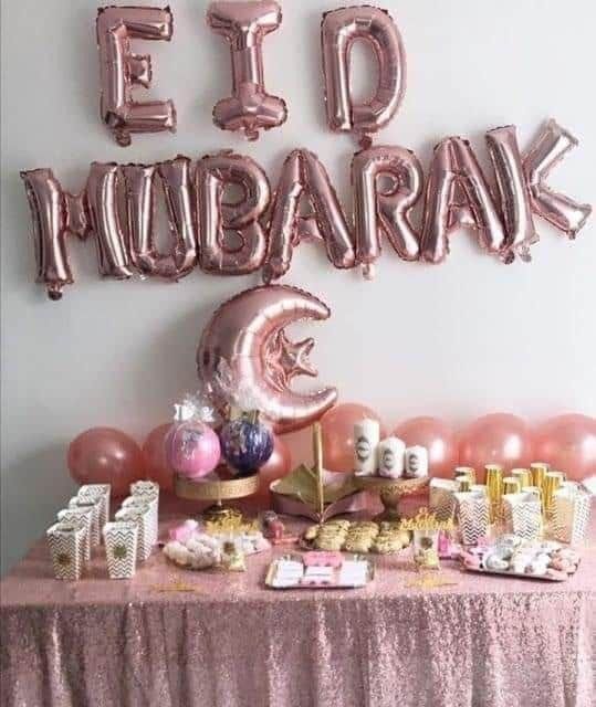 a pink table topped with lots of balloons and other items next to a sign that says eid mubarak