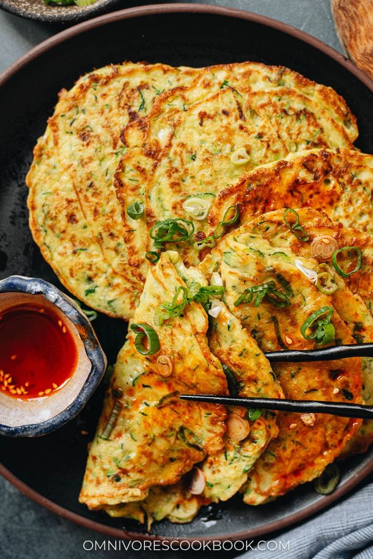 an omelet with chopsticks and dipping sauce on the side in a bowl