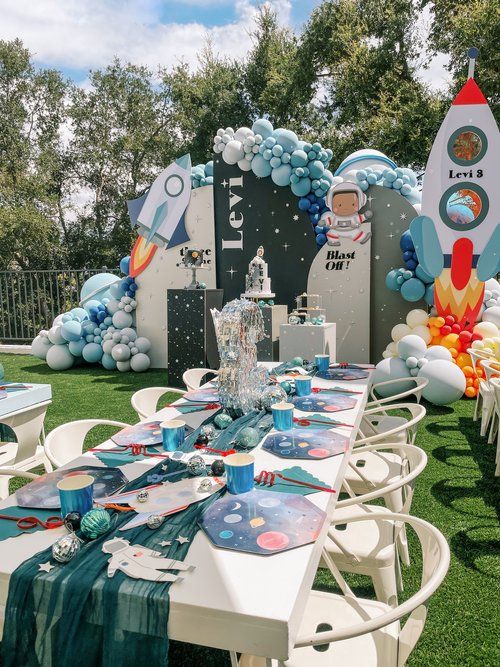 a table set up for an outer space themed birthday party with balloons and rocket ship decorations