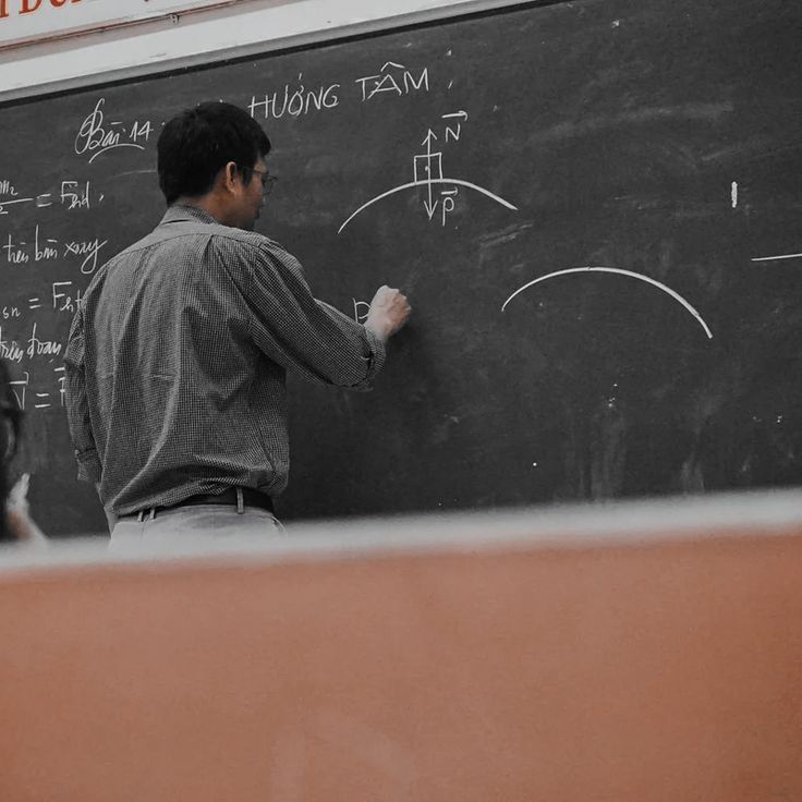 a man writing on a blackboard in front of another man who is standing next to him