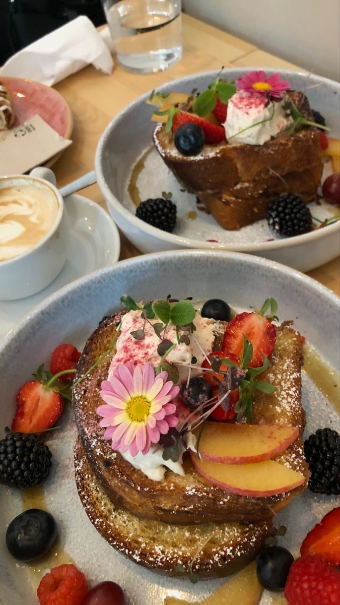 two white plates topped with french toast covered in fresh fruit and flowers on top of a wooden table