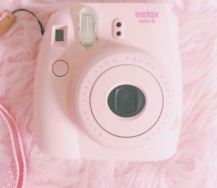 an instax camera sitting on top of a pink blanket