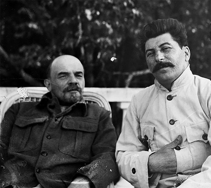 two men sitting next to each other on a park bench in front of some trees