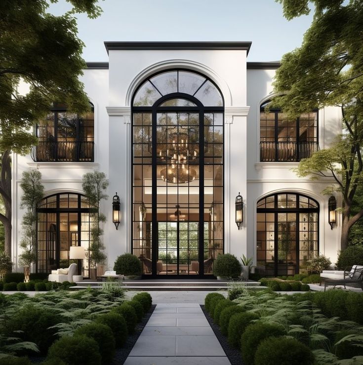 a large white house with lots of windows and plants on the front lawn, surrounded by greenery