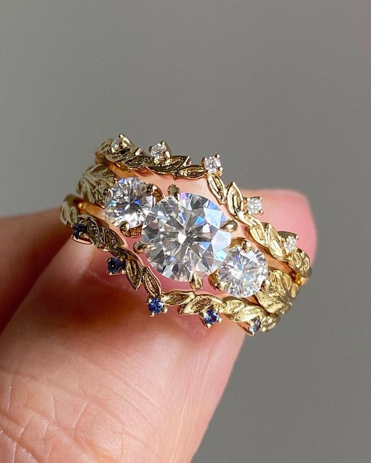 a close up of a person's hand holding a gold ring with three stones