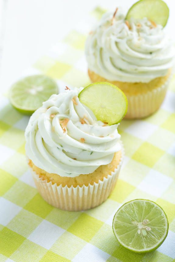 two cupcakes with white frosting and lime slices