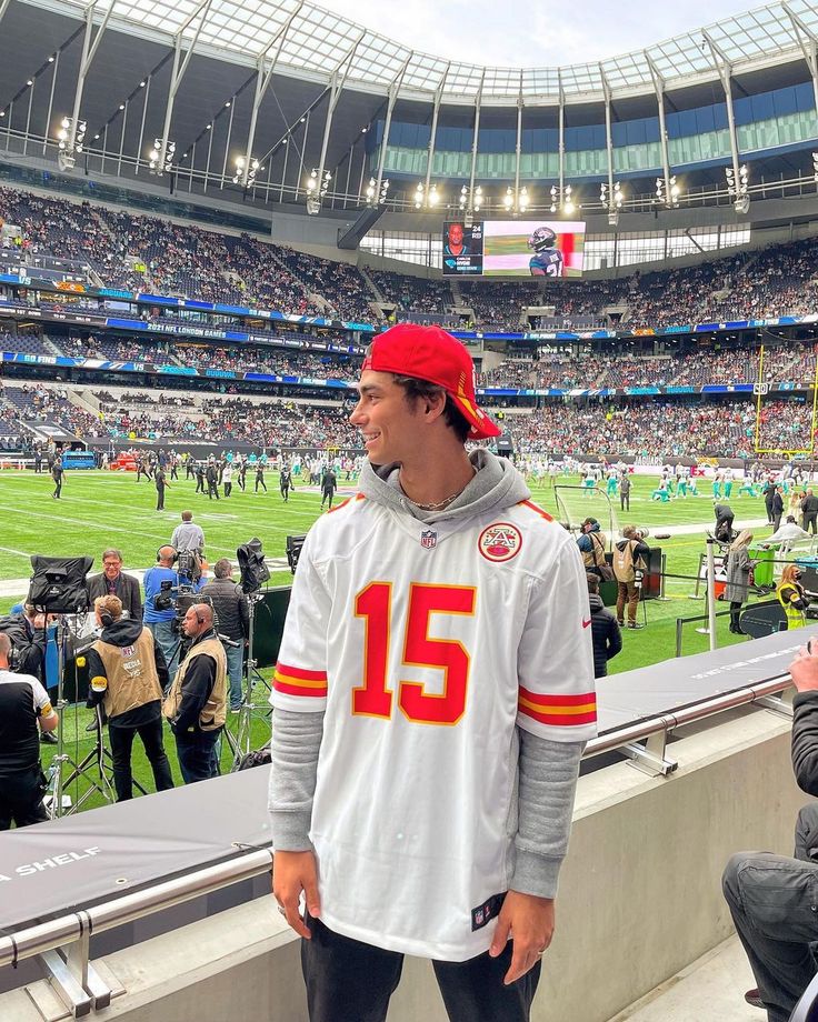 a man standing in front of a crowd at a football game wearing a jersey with the number 15 on it