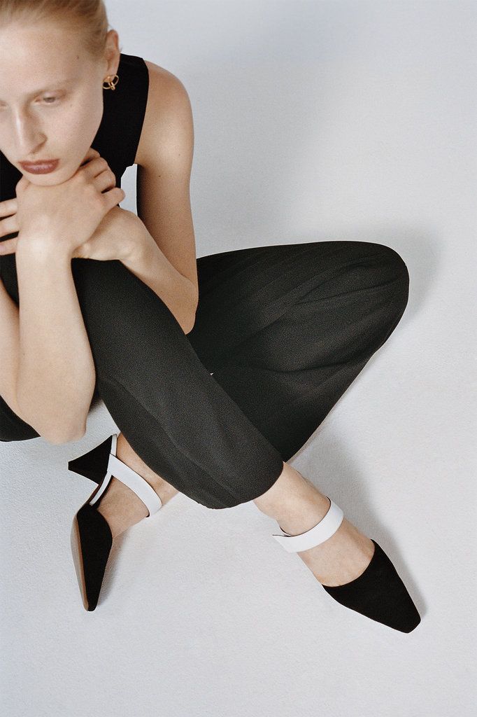 a woman is sitting on the floor with her legs crossed wearing black and white shoes