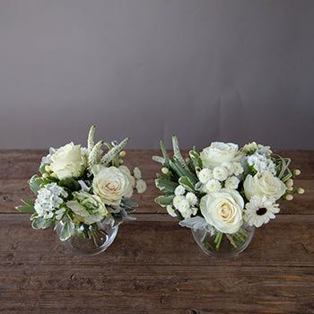 two clear vases filled with white flowers on top of a wooden table next to each other