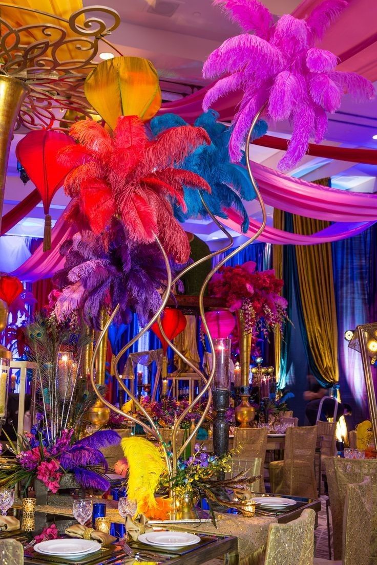 an elaborately decorated dining room with colorful feathers and flowers on the table, in front of hanging chandeliers