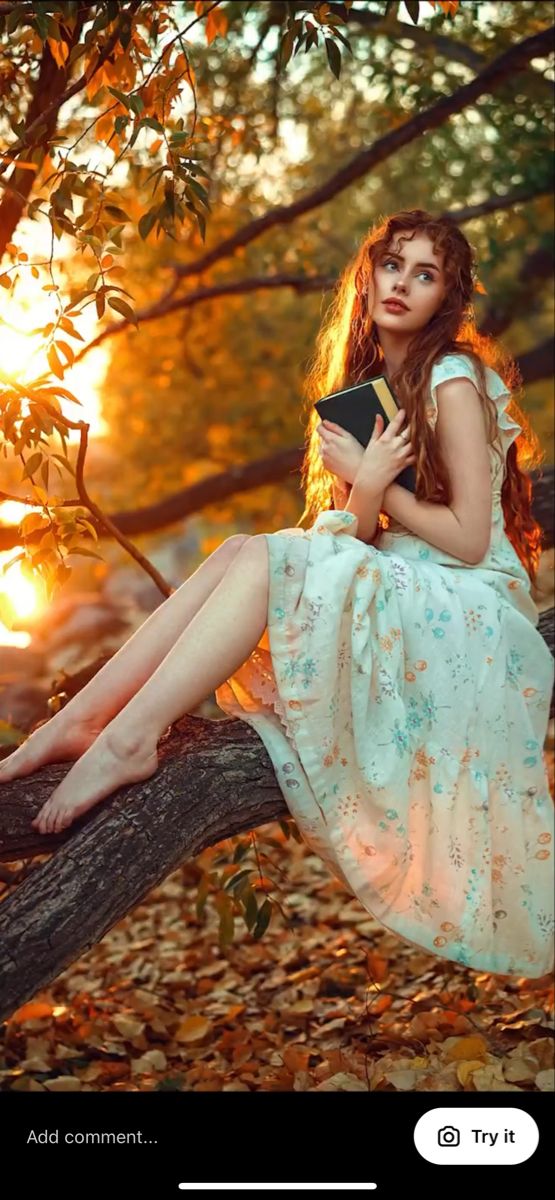 a woman in a dress sitting on a tree branch holding a book and looking at the camera