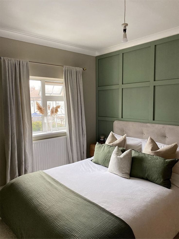 a bedroom with green paneled walls and white bedding, along with two windows