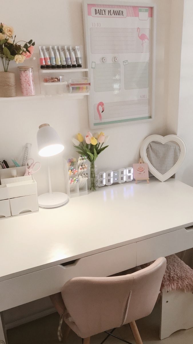 a white desk topped with a lamp next to a pink chair and vase filled with flowers