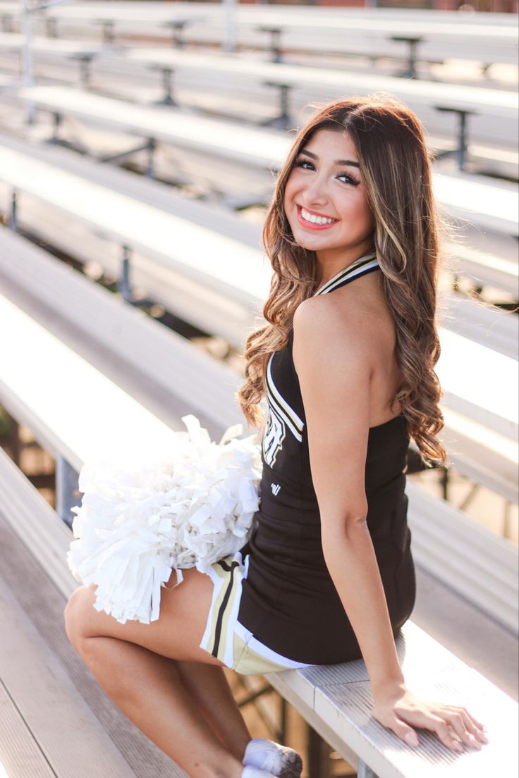 a beautiful young woman sitting on top of a bench holding a cheerleader pom pom