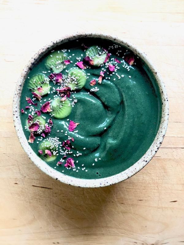 a green smoothie in a bowl with sprinkles and flowers on top